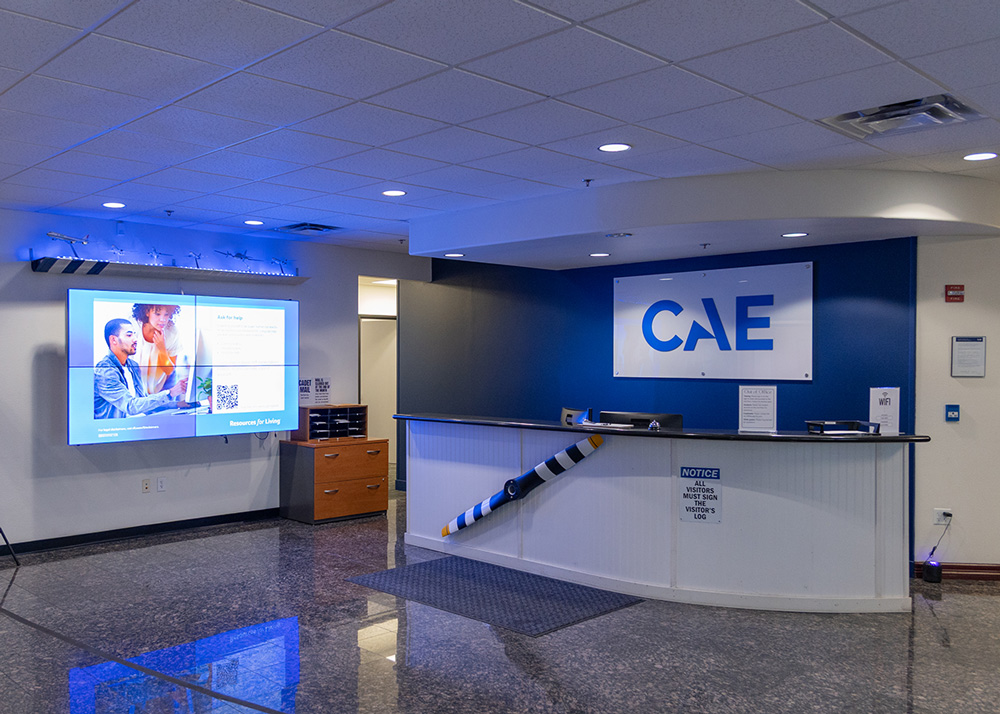 CAEメサ校エントランスホール。受付カウンターと壁面に掲げられたCAEロゴ、デジタルサイネージが設置された清潔感のあるロビーの画像