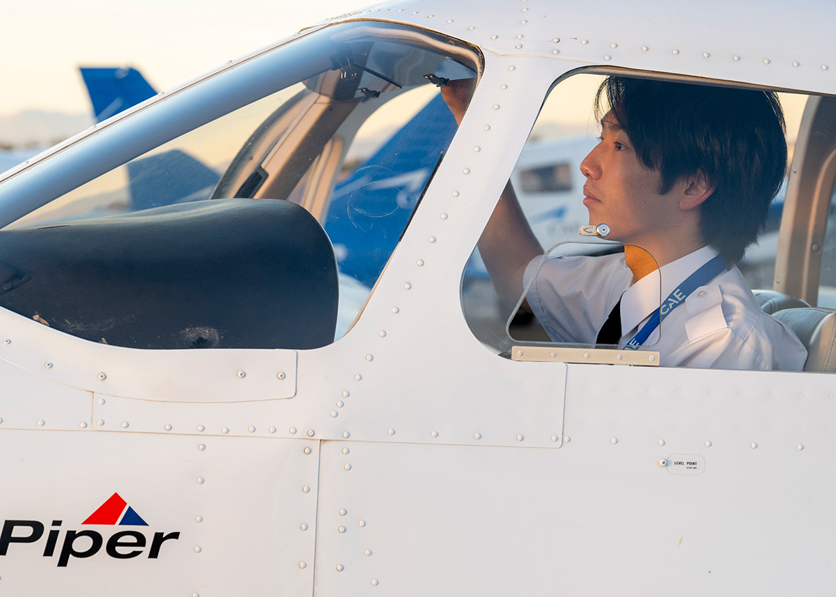 夕日を浴びるPiper訓練機のコックピットで、出発前のチェックを行うパイロット訓練生の横顔の画像