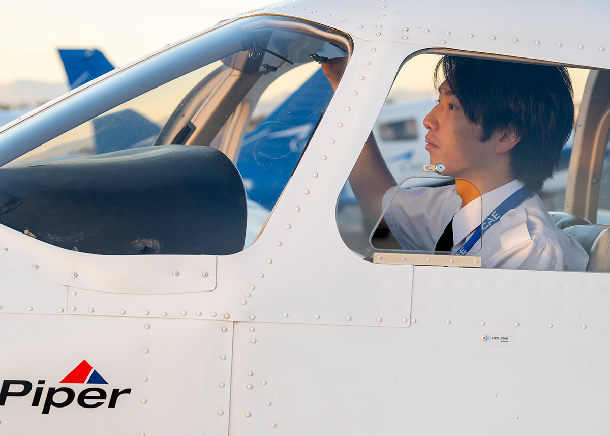 夕日を浴びるPiper訓練機のコックピットで、出発前のチェックを行うパイロット訓練生の横顔の画像