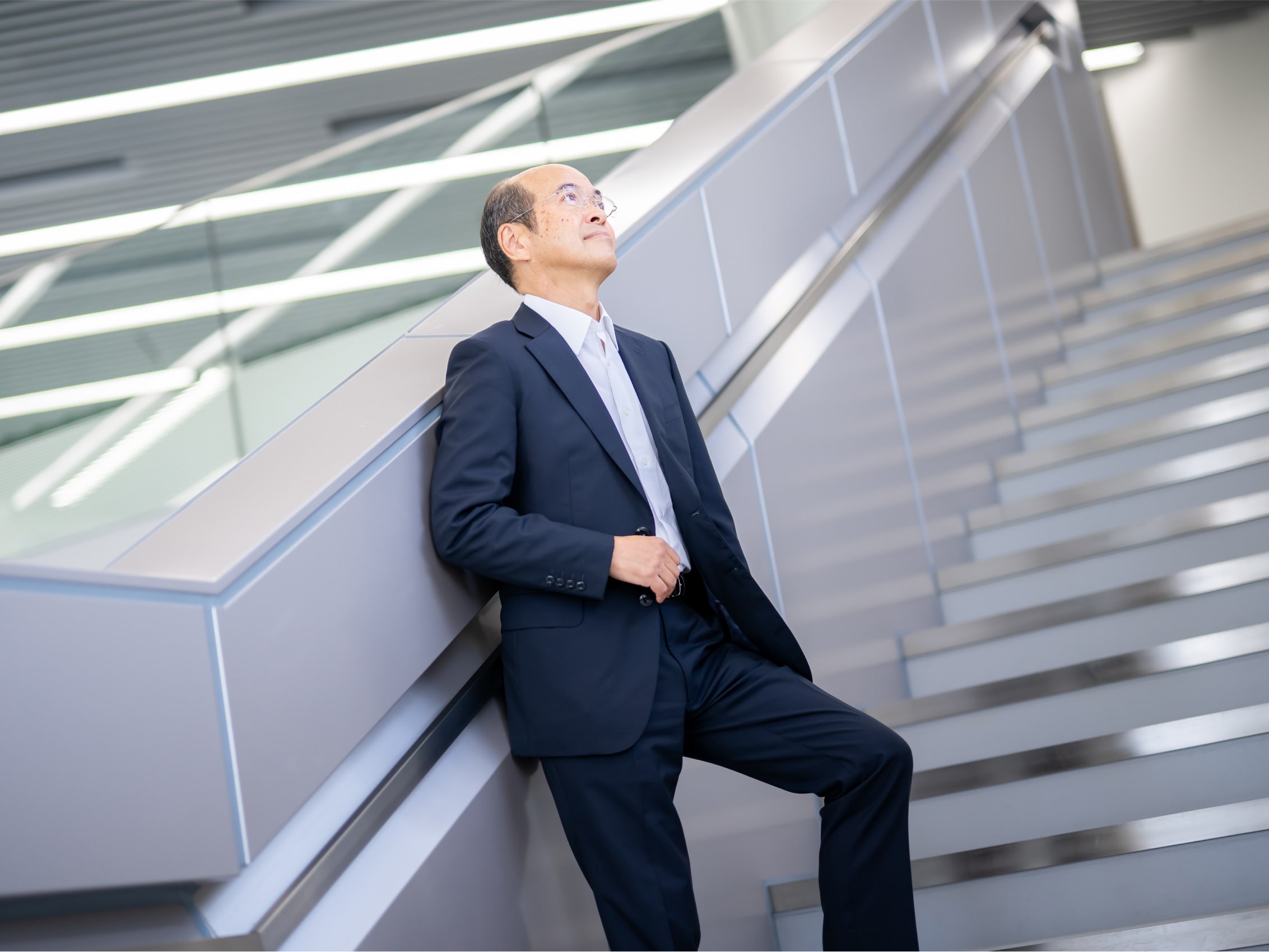 階段で上を見上げる堤正行先生