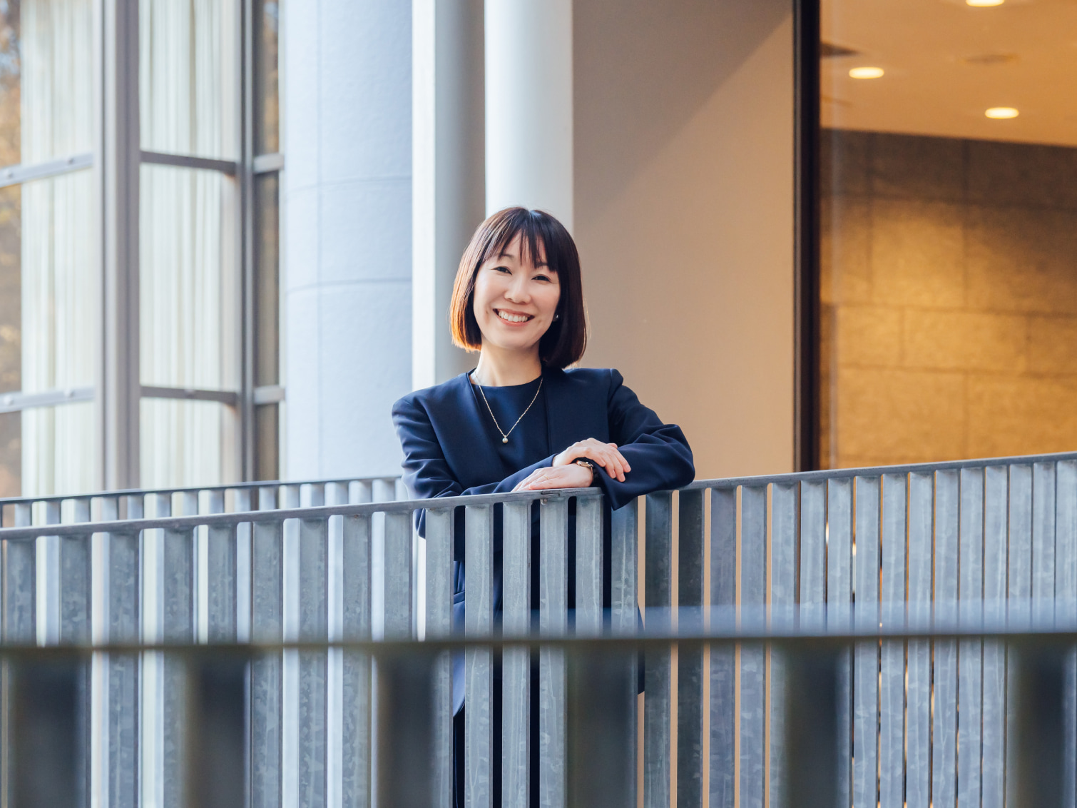 手すりに寄りかかり笑顔を見せる神庭直子先生